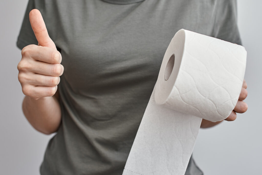 Woman hand hold toilet paper roll and show thumb up gesture, close up. Hygiene concept