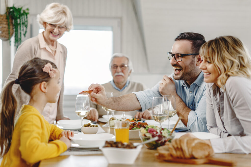 Multi-generation family having fun during lunch while father is feeding his little girl at dining table.
